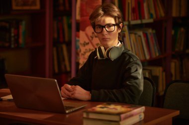 Akıllı bir öğrenci bir kütüphanede dizüstü bilgisayarla masada oturuyor. Eğitim. Modern öğrenciler.