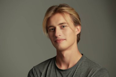 Gri stüdyo arka planında sarı saçlı, gülümseyen genç bir adamın portresi. Mutlu insanlar. Erkeklerin güzelliği ve sağlığı.