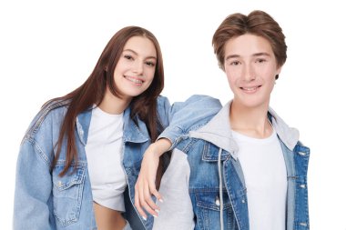 Beyaz arka planda poz veren şık kot elbiseli, gülümseyen genç erkek ve kız portresi. Denim tarzı, gençlik tarzı..