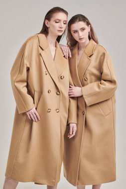 Uzun bej keçeli ceketlerle poz veren iki güzel model kızın portresi. Beyaz stüdyo geçmişi. Yarı sezon modası.