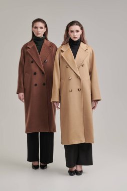 Yarı sezon kadın modası. Fiyakalı keçeli paltolarla poz veren iki model kızın tam boy portresi. Stüdyo beyaz arkaplan.