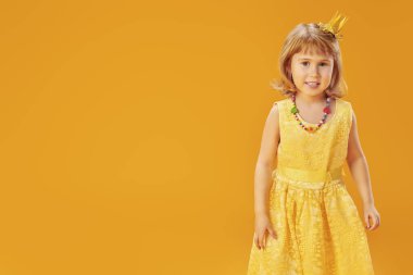 Güzel bir çocuk kostüm partisi ya da doğum günü için hazırlanıyor. Prenses elbisesi ve taç giymiş şirin küçük bir kız. Çocuk modası. Stüdyonun sarı arka planında metin için yeri olan bir portre.