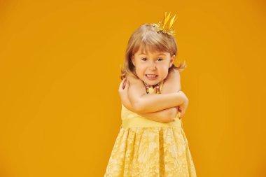 Sarı elbiseli, kaprisli küçük bir prenses ve altın bir taç çok kızgın. Çocuk duyguları. Stüdyo sarı arkaplan ve metin için boşluk.