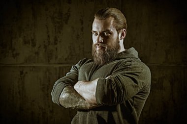 Erkeklik ve fiziksel güç kavramı. Siyah kapüşonlu, beton duvara dayanmış kaslı, sakallı bir adamın portresi.. 