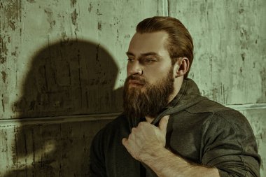 Erkeklerin gücü. Beton duvara karşı siyah kapüşonlu, iri yarı, sakallı bir adamın portresi. Erkeklik ve fiziksel güç kavramı..