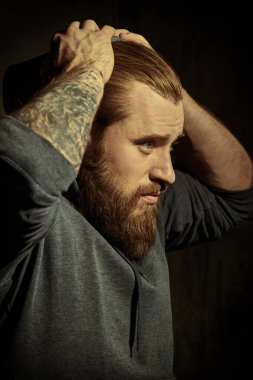 Siyah arka planda gri kapüşonlu, iri yarı, sakallı bir adamın portresi. Erkeklik ve fiziksel güç kavramı..