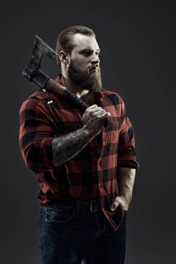 Omzunda balta tutan ekose gömlekli vahşi sakallı bir adamın portresi. Koyu gri stüdyo geçmişi. Erkek güzelliği ve erkeklik.