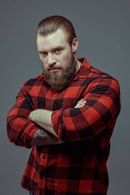 Gri bir stüdyo arka planında ekose gömlekli, sakallı yakışıklı bir adamın portresi. Erkek güzeli. Berber dükkanı reklamı. Erkeklik ve güç.