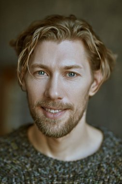 Kıvırcık saçlı, sıradan örgü süveter giymiş ve kameraya bakan 40 yaşında yakışıklı bir adamın portresi. Çatı katı. İnsanlar, duygular. Erkek güzeli..