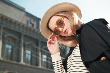 Moda modası geçmiş siyah trençkotlu, beyaz şapkalı ve güneş gözlüklü bir şehir caddesinde poz veren modern genç kadın model. Moda ve tarz. Metin için yer.