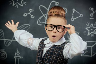 Eğitici bir kavram. Okul üniformalı ve gözlüklü şirin bir kızın portresi şaşırmış görünüyor. Bilimsel çizimleri olan siyah bir kara tahta. Genç bilim adamları.