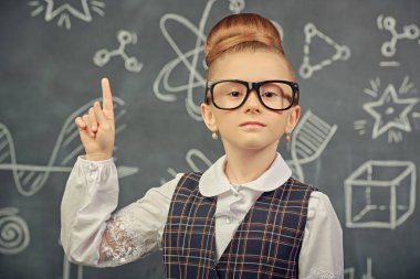 Eğitici bir kavram. Okul üniformalı, gözlüklü ve kameraya özgüvenle bakan zeki bir kızın portresi. Bilimsel çizimleri olan siyah bir kara tahta. Genç bilim adamları.