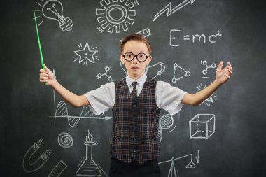 Okul üniformalı, gözlüklü ve kameraya bakan zeki bir çocuğun portresi. Bilimsel çizimleri olan siyah bir kara tahta. Eğitim. Genç bilim adamları.