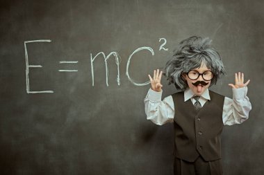 Alışılmışın dışında düşün. Gözlüklü, bıyıklı, peruklu, küçük Einstein gibi sevimli bir çocuk dilini dışarı çıkarıyor. Siyah karatahta arka planı. Eğitim ve erken kalkınma.