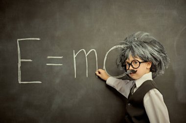 Gözlüklü, bıyıklı ve peruklu sevimli bir çocuk, küçük Einstein gibi, bir formül yazıyor. Kopya alanı olan siyah karatahta arkaplan. Eğitim ve erken kalkınma.