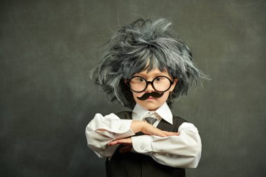 Gözlüklü, bıyıklı ve peruklu şirin bir çocuk. Tıpkı küçük profesörün kameraya bakışı gibi. Kopya alanı olan siyah bir karatahtanın arka planı. Eğitim. Küçük Bilim Adamı.