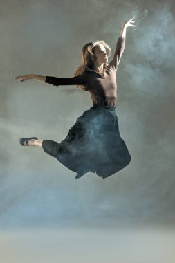 Stüdyoda karanlık bir arka planda poz veren genç dansçı kız. Etrafı sisli. Modern dans tarzı. Tam boy portre.
