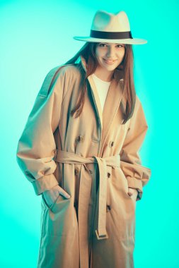 Güzel esmer bir kızın şık kahverengi bir trençkot ve beyaz keçeli bir şapka giyip kameraya güvenle baktığı bir fotoğraf. Güzellik portresi. Moda, yarı sezon kıyafetleri ve aksesuarlar..