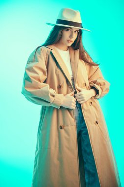 Moda, yarı sezon kıyafetleri ve aksesuarlar. Güzel esmer bir kızın portresi şık kahverengi bir trençkot ve beyaz keçeli bir şapka giymiş, kendine güvenen. Güzel portre..