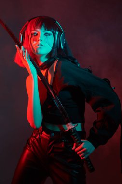 Siber dünya konsepti. Cesur bir sayborg samuray kızı elinde bir kılıçla ateş kıvılcımlarının kırmızı yansımalarıyla ayakta duruyor. Oyun, sanal gerçeklik.
