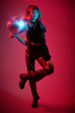 Disko siber punk kızı. Parlak kırmızı makyajlı ve şık kızıl saçlı çekici kız disko topuyla neon kırmızısı ve mavi ışıkta poz veriyor. Gece partisi.  