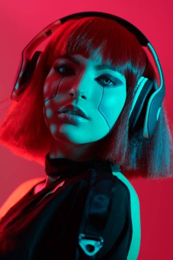 Kulaklıklı çekici bir siber punk kızı kırmızı ışıkta kırmızı arka planda poz veriyor. Bilim kurgu cyborg kızı. Oyun, sanal gerçeklik. 