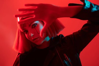 Çekici bir siber punk kızı kırmızı ışıkta kırmızı arka planda poz veriyor. Bilim kurgu cyborg kızı. Oyun, sanal gerçeklik. 