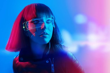 Parlak kırmızı makyajlı ve kızıl saçlı şık bir siber kızın portresi karışık neon ışıkta duruyor. Siber punk konsepti. Fütürist teknoloji tarzı. VR oyunları. Boşluğu kopyala.