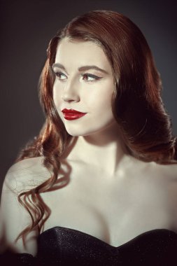 Akşam saçı ve makyajı. Uzun dalgalı saçlı güzel bir kızın portresi ve kırmızı dudaklı parlak bir akşam makyajı, yakalı siyah bir elbise içinde poz veriyor. Stüdyo çekimi.