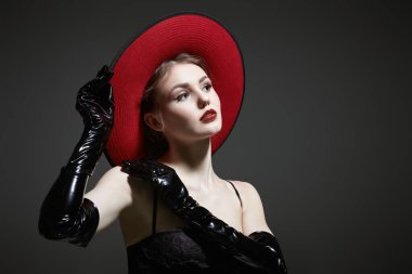 Gece makyajlı, şapka, korse ve siyah lateks eldiven giymiş güzel siyah saçlı bir kızın portresi. Moda fotoğrafı. Gri arkaplanda fotokopi alanı olan bir stüdyo portresi.