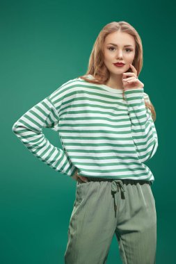 Yeşil pantolonlu ve yeşil çizgili uzun kollu mutlu güzel kız. Yeşil arka planda stüdyo portresi. Aziz Patrick Günü kutlaması. Sıradan moda..