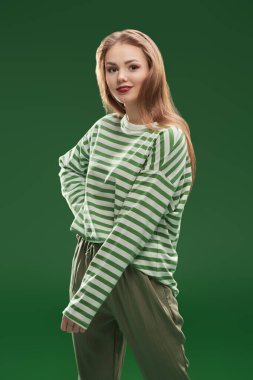 Yeşil pantolonlu, yeşil çizgili uzun kollu dans eden ve eğlenen mutlu güzel kız. Yeşil arka planda stüdyo portresi. Aziz Patrick Günü kutlaması.