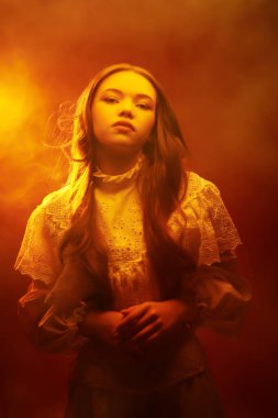 Güzel, romantik bir kız. Uzun dalgalı saçları var. Beyaz, eski moda bir elbiseyle poz veriyor. Koyu kırmızı stüdyo.