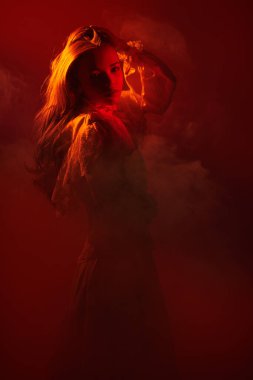 Güzel, romantik bir kız. Uzun dalgalı saçları var. Beyaz, eski moda bir elbiseyle poz veriyor. Koyu kırmızı stüdyo.