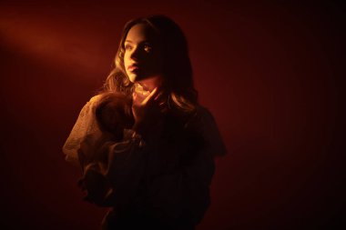 Beyaz bir elbise içinde poz veren uzun dalgalı saçlı güzel romantik bir kız. Fotokopi alanı olan koyu kırmızı bir stüdyo. Bir insanın iç dünyası, duyguları ve duyguları..