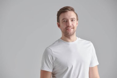 İnsanlar, duygular. Beyaz tişörtlü, pozitif, orta yaşlı bir adamın portresi yana bakıyor. Erkek sağlığı ve güzelliği. Fotokopi alanı ile gri bir arkaplanda stüdyo resmi. 