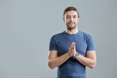 Pozitif orta yaşlı mavi tişörtlü bir adam kameraya bakıyor ve gülümsüyor. Erkek sağlığı ve güzelliği. Gri arkaplanda fotokopi alanı olan bir stüdyo resmi. İnsanlar, duygular. 