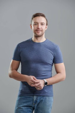 Mavi tişörtlü, sakin, orta yaşlı bir adamın portresi. Erkek sağlığı ve güzelliği. Gri bir arkaplanda stüdyo resmi. İnsanlar, duygular. 