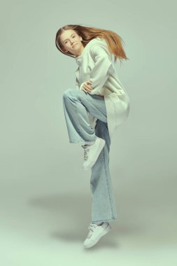 Beyaz bir kapüşonlu ve kot pantolonla beyaz bir stüdyoda poz veren güzel bir genç kız. Aktif gençlik yaşam tarzı. Dans eden kız. Hip-hop ve modern dans.