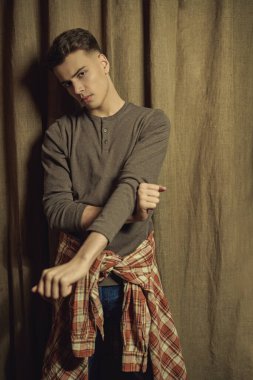 Gri kazaklı yakışıklı bir gencin portresi kahverengi perde arkasında. Gençlik modası. Erkek güzeli, saç stili. Stüdyo resmi.