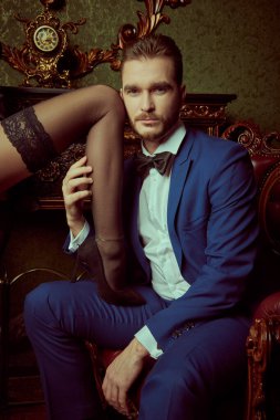 Bir adam lüks dairelerde sevgilisinin bacağını tutkulu bir şekilde kucaklayarak kız arkadaşıyla flört eder. Aşk ve tutku. Akşam Moda..