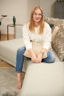 Evdeki rahat bir oturma odasında poz veren gözlüklü mutlu orta yaşlı kadın. Mutlu bir yaşam tarzı. Gözlük modası. 