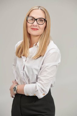 Klasik resmi kıyafet ve gözlüklerle kameraya bakıp gülümseyen orta yaşlı mutlu bir iş kadını fotoğrafı. Gözlük stili. Gri stüdyo geçmişi. 