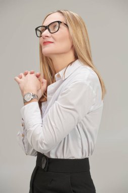 Klasik resmi kıyafet ve gözlüklerle kameraya bakıp gülümseyen orta yaşlı mutlu bir iş kadını fotoğrafı. Moda ve gözlük tarzı. Gri stüdyo geçmişi. 