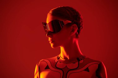 Fütürist aynalı gözlüklü ve tulumlu mükemmel siber punk kızı kırmızı ışık ve ateş yansımaları içinde duruyor. Geleceğin siber dünyası. Sanal oyunlar.