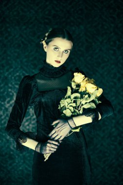 Zarif siyah kadife elbiseli dramatik bir esmer kız gecenin karanlığında elinde bir buket solmuş gülle arka planda duruyor. Gotik roman, mistisizm.. 