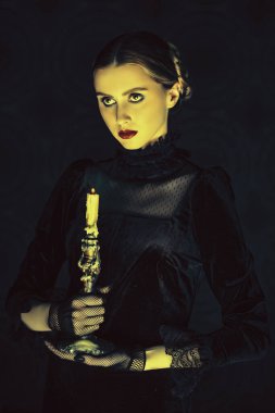 Zarif siyah kadife elbise ve dantel eldivenli dramatik bir esmer kızın portresi, gecenin karanlığında elinde mumla dikiliyor. Gotik roman, mistisizm..