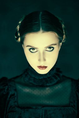 Siyah kadife elbiseli dramatik esmer bir kızın portresi, gecenin karanlığında eskimiş bir arka planda duruyor. Gotik roman, mistisizm. Makyaj ve saç stili.
