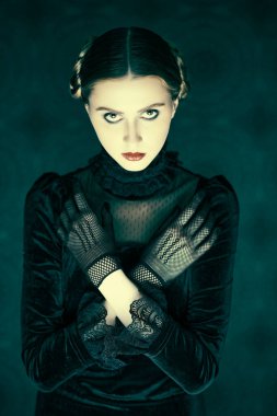 Şık siyah kadife elbise ve dantel eldiven giymiş esmer bir kızın portresi, gecenin karanlığında eskimiş bir arka planda duruyor. Gotik roman, mistisizm. Makyaj ve saç stili.