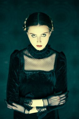 Gotik roman, mistisizm. Şık siyah kadife elbise ve dantel eldiven giymiş esmer bir kızın portresi, gecenin karanlığında eskimiş bir arka planda duruyor. Makyaj ve saç stili.